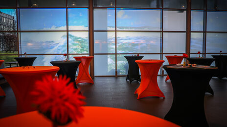 Photo of many decorated bar tables with black and orange covers standing in front of a wall onto which waves are projected.